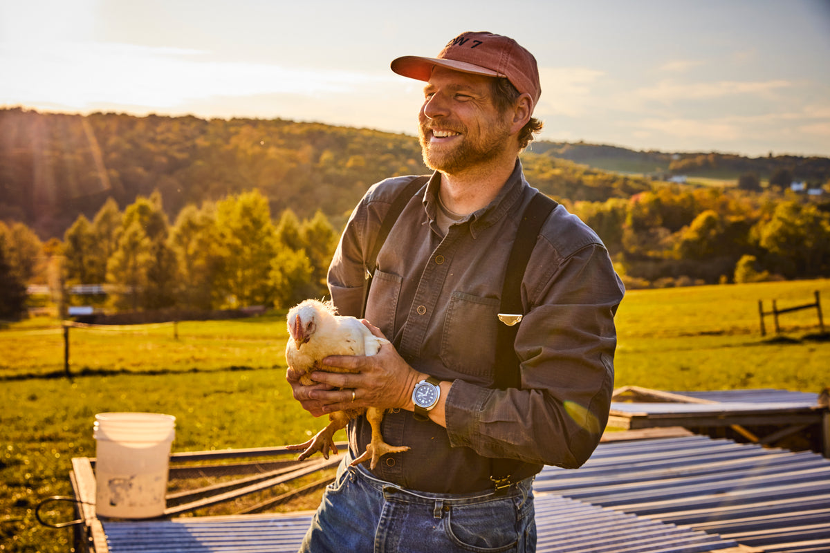 Ryan holding a chicken on the pasture at golden hour